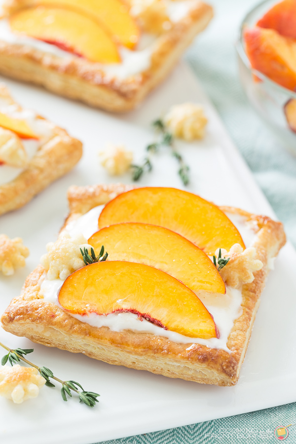 This peach tart recipe is bursting with fresh peaches, a creamy filling on a delicate puffed pastry! a peach tart on a white ceramic tray