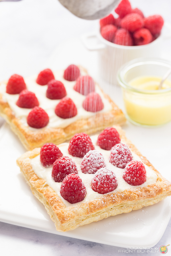 two raspberry lemon tarts sprinkling powdered sugar on them