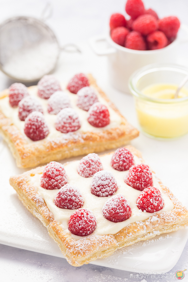 two raspberry lemon tarts with powdered sugar on a white plate