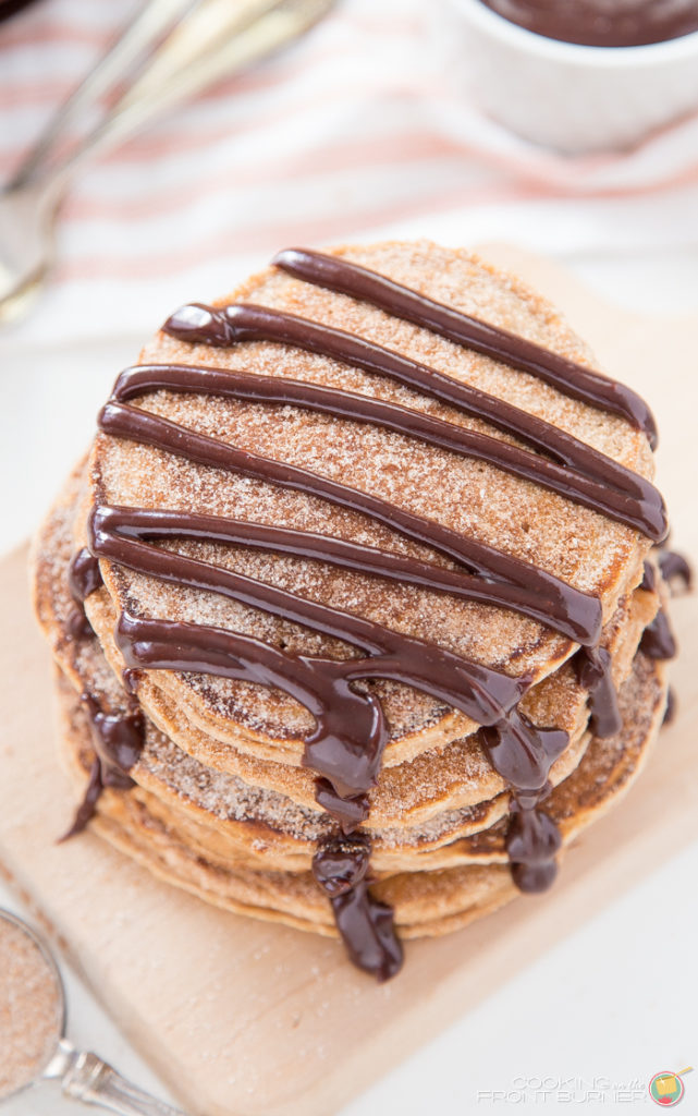 5 churro pancakes stacked on a board with chocolate sauce