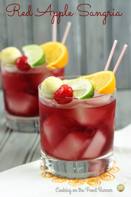 two red apple sangrias in short old fashioned glasses topped with orange, lime, cherry