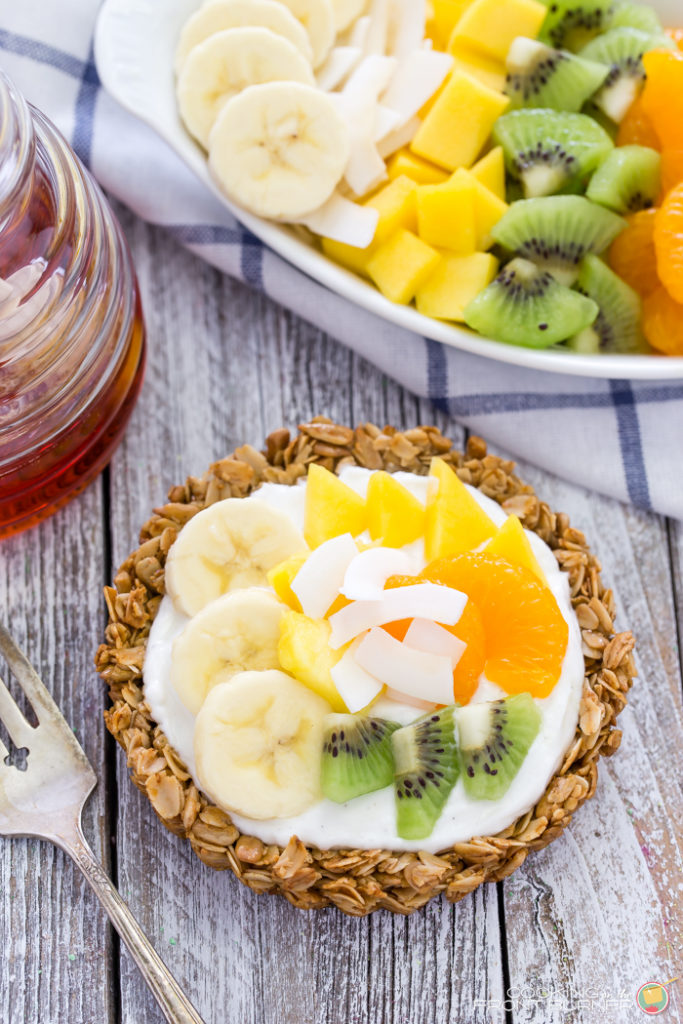 Breakfast granola tarts with creamy vanilla yogurt, topped with tropical fruits and drizzled with golden honey.
