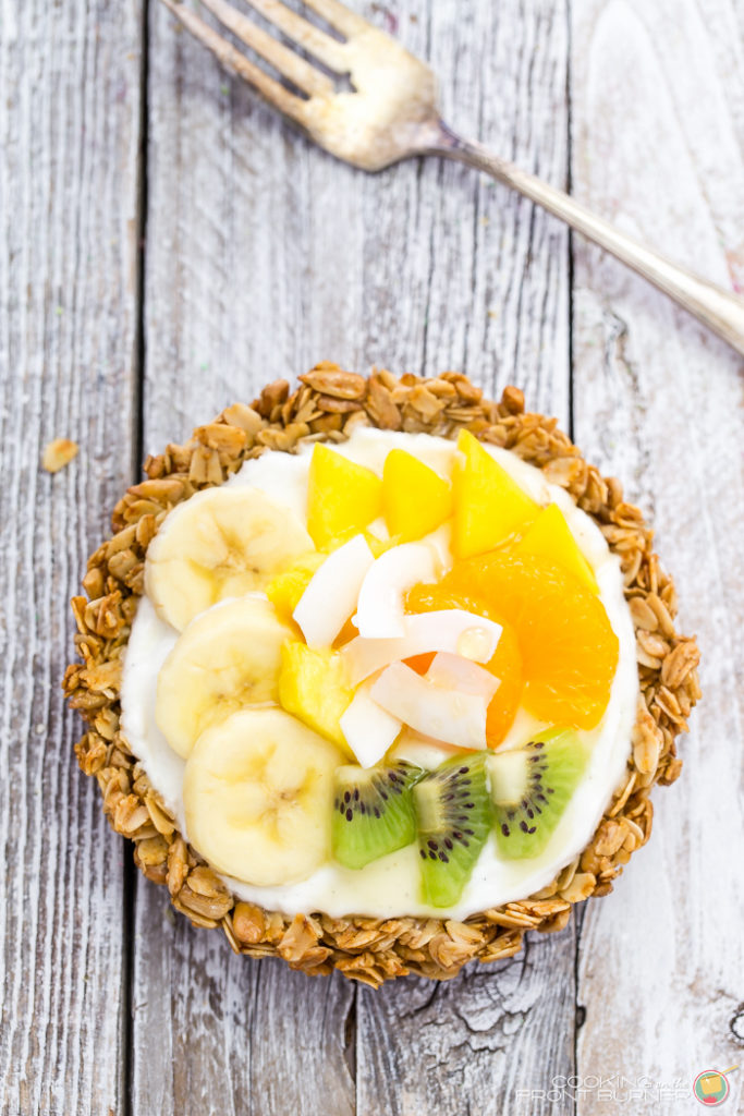 Breakfast granola tarts with creamy vanilla yogurt, topped with tropical fruits and drizzled with golden honey.