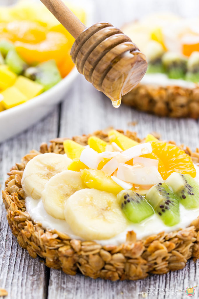 Breakfast granola tarts with creamy vanilla yogurt, topped with tropical fruits and drizzled with golden honey.