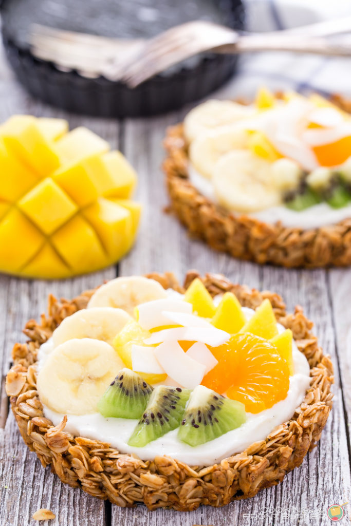 Breakfast granola tarts with creamy vanilla yogurt, topped with tropical fruits and drizzled with golden honey.