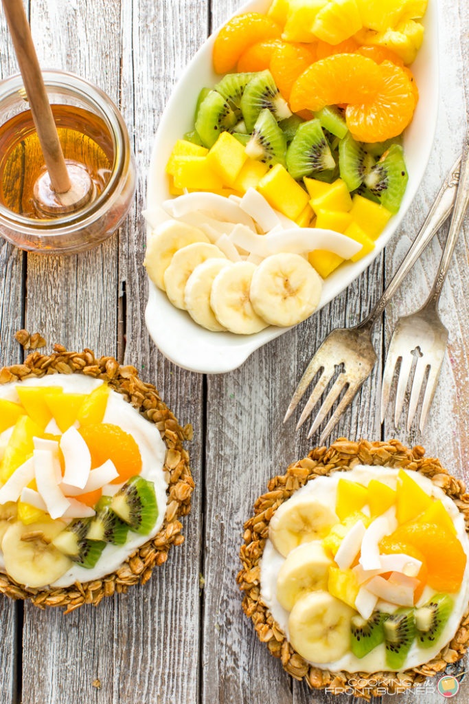 Breakfast granola tarts with creamy vanilla yogurt, topped with tropical fruits and drizzled with golden honey.