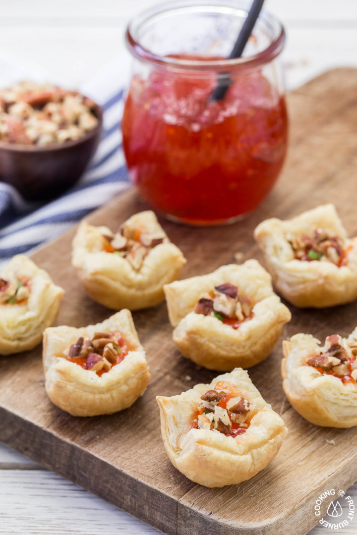 puff pastry appetizers on a board with a jar of hot pepper jelly next to it