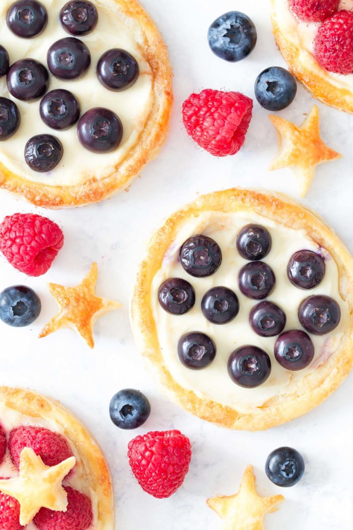 3 breakfast pastries on a board with fresh blueberries and raspberries next to them
