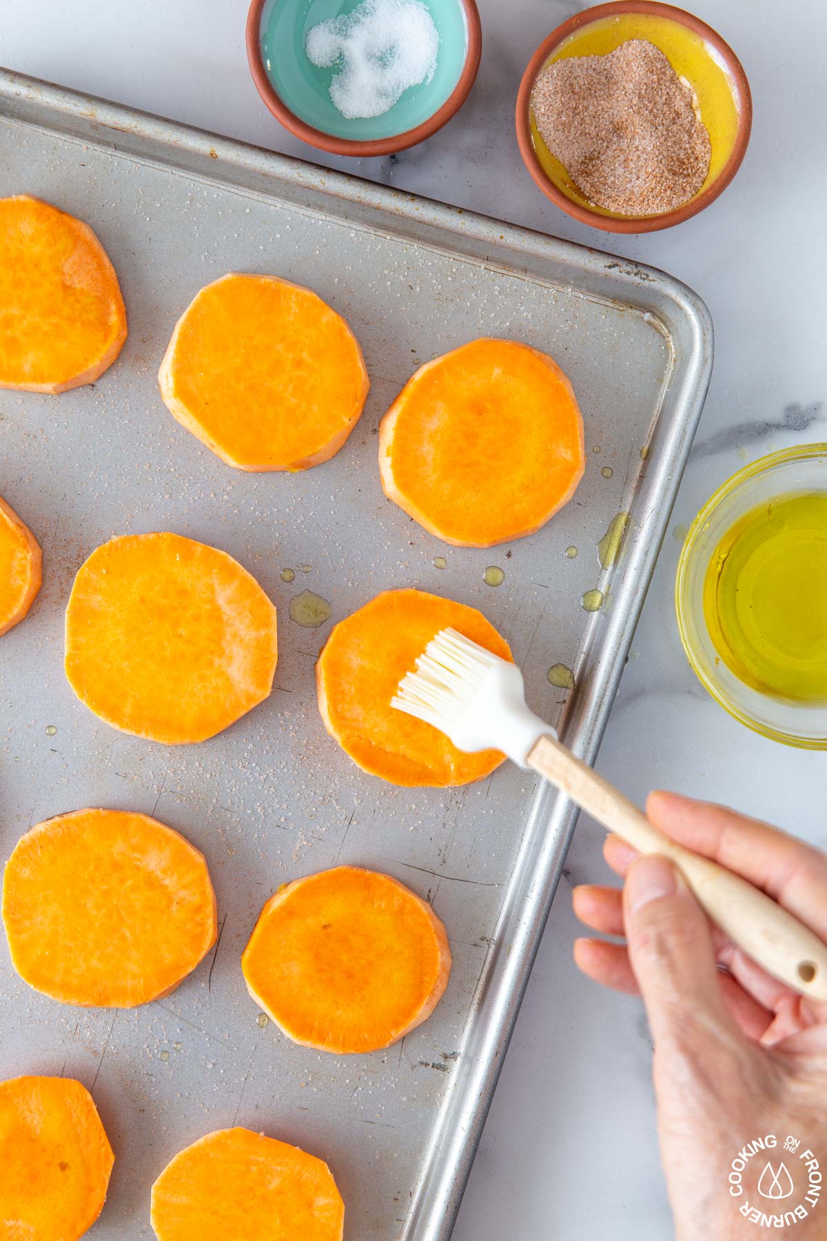 brushing olive oil on sweet potato rounds on a cookie sheet