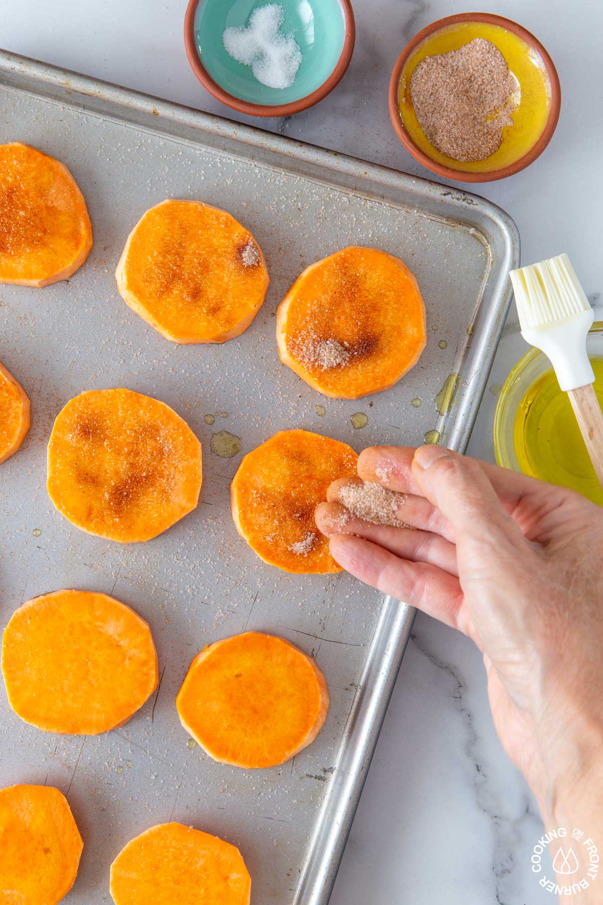 sprinkling cinnamon-sugar mixture on sweet potato rounds