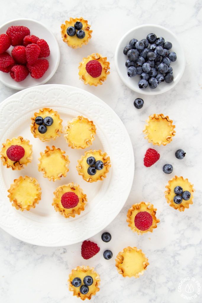 tarts on a plate with bowls of raspberries and blueberries