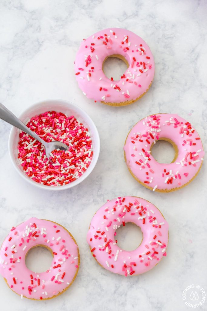 4 donuts sitting next to a bowl of sprinkles