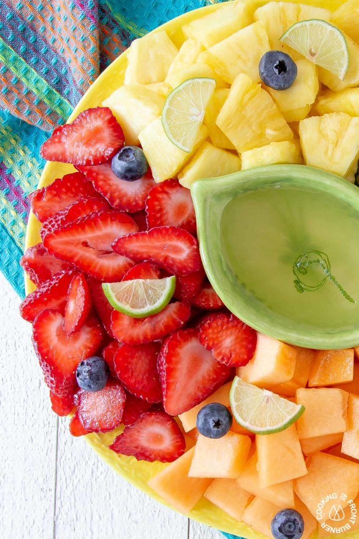 a green dish with simple syrup on a yellow platter with fresh fruit cut up