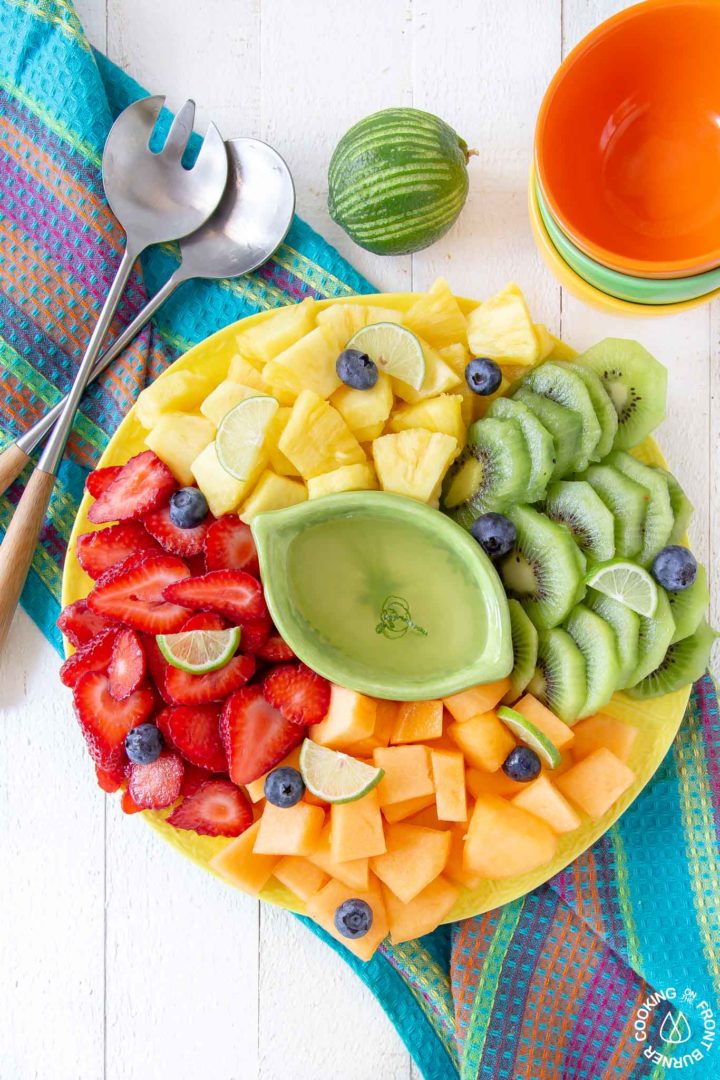 a yellow platter with cut fresh fruit on a striped towel
