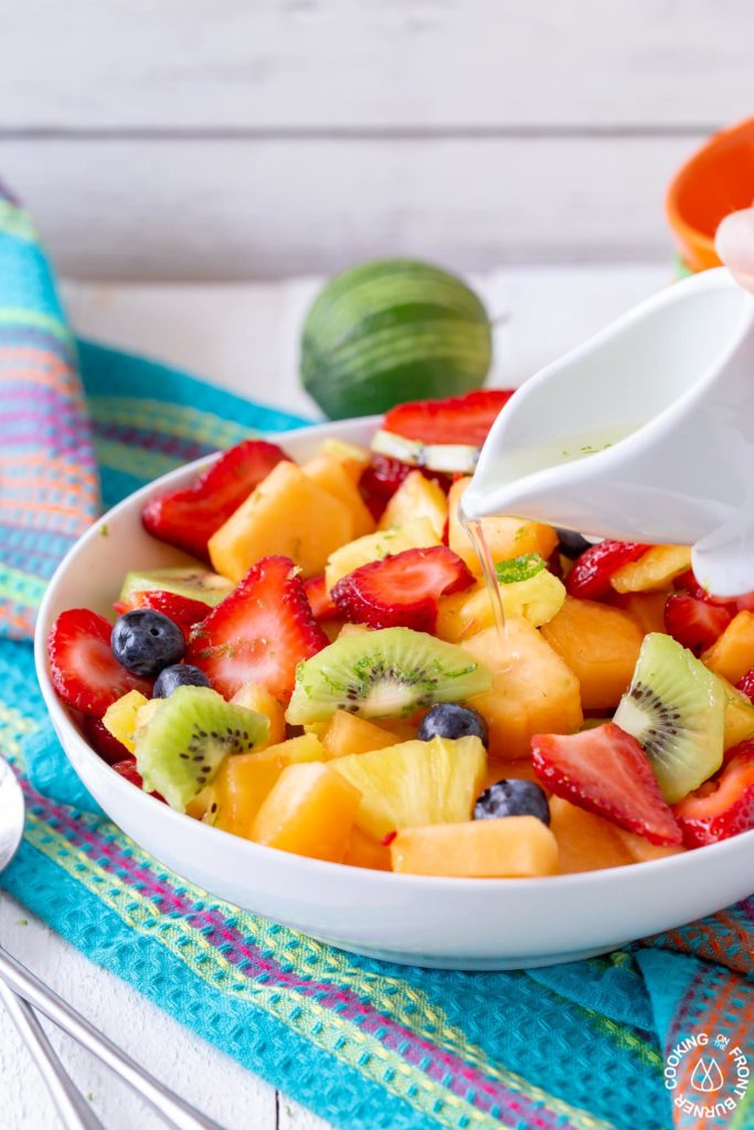 fresh fruit in a white bowl with a white container pouring simple syrup