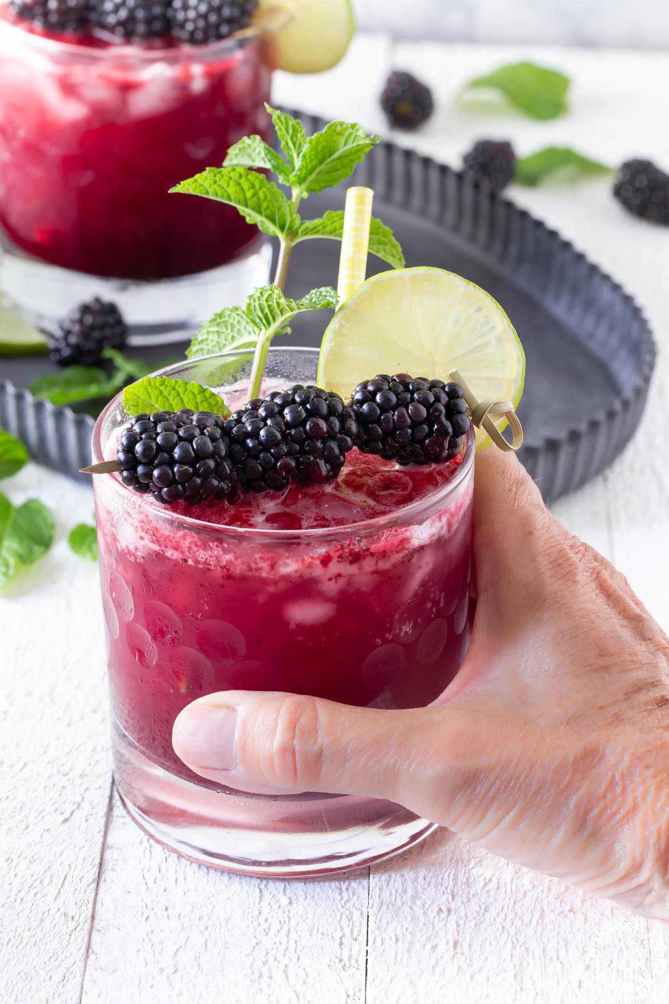 a hand holding a blackberry bramble in a clear glass