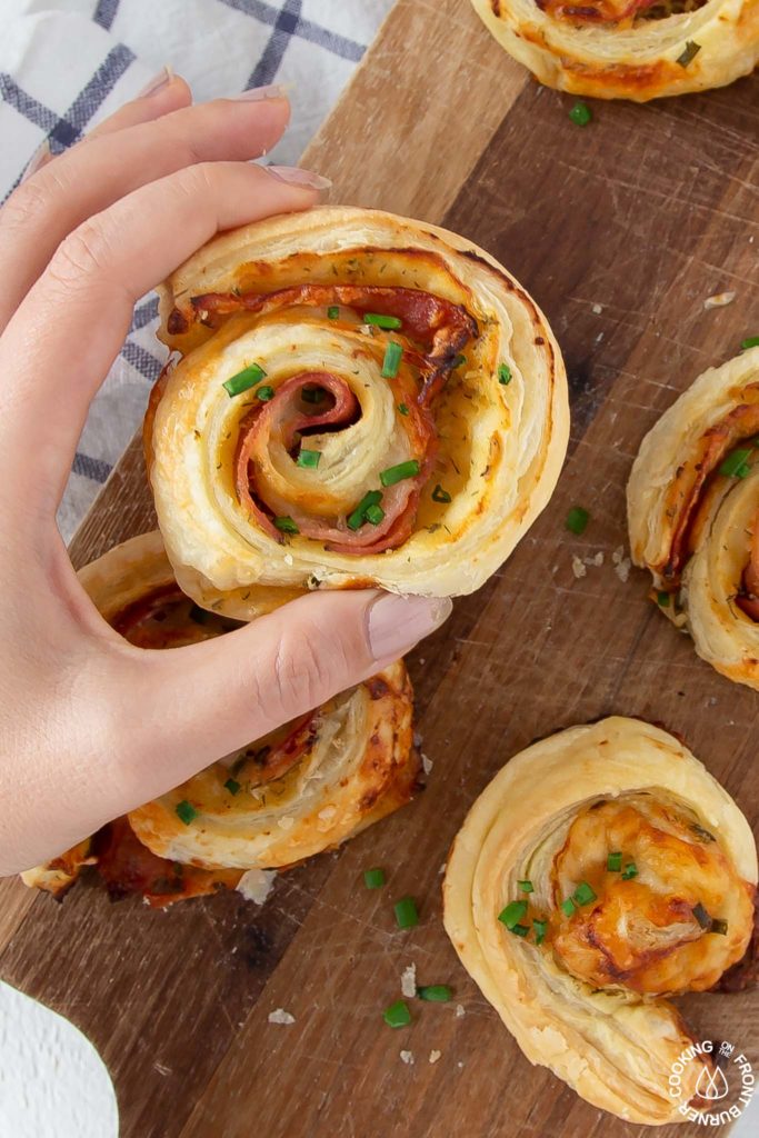 a hand holding a ham cheese pinwheel with chives on top