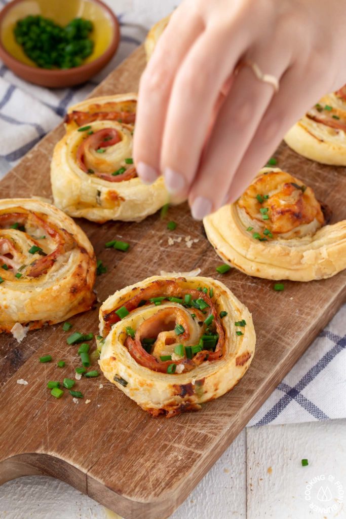 sprinkling chives on a ham cheese puff pastry pinwheel