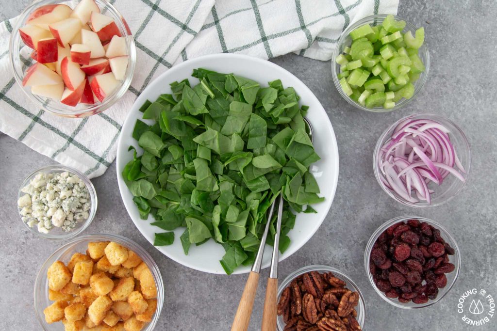 a bowl of spinach with salad ingredients around the bowl