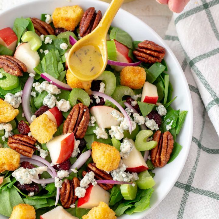 chopped spinach salad in a bowl with a drizzle of maple vinaigrette