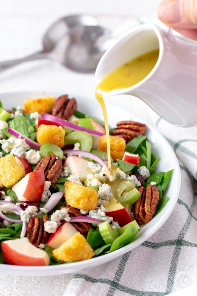 a chopped spinach salad mixed in a bowl with maple dressing being drizzled