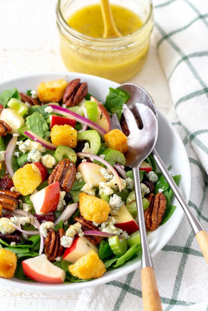 spinach salad with serving utensils in a bowl