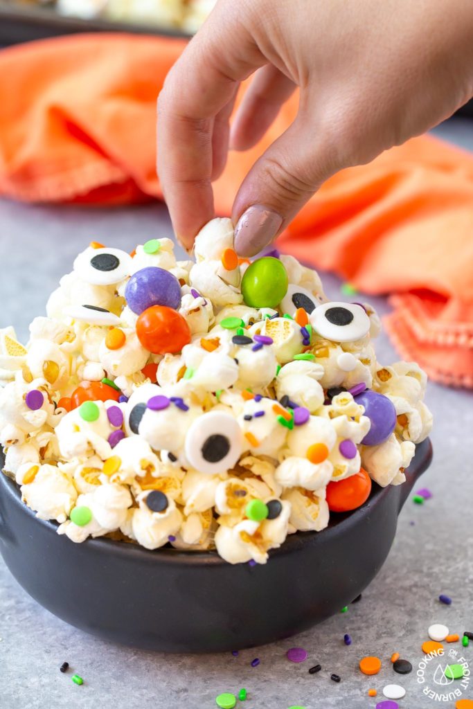 a hand taking a piece out of bowl of halloween snack mix