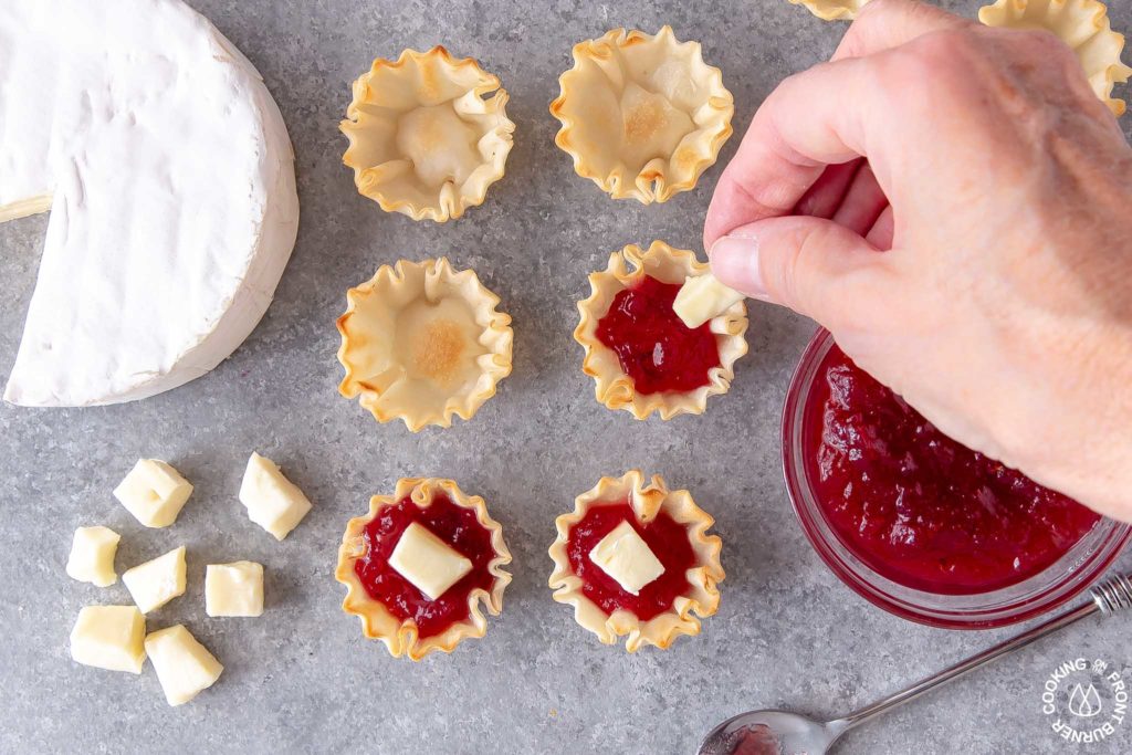 a hand placing a piece of brie cheese in a phyllo cup