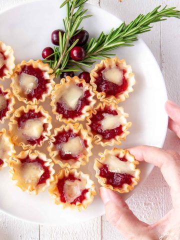 cranberry orange brie tarts on a plate with a hand taking one off