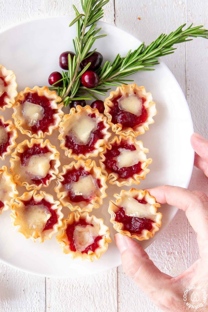 cranberry orange brie tarts on a plate with a hand taking one off
