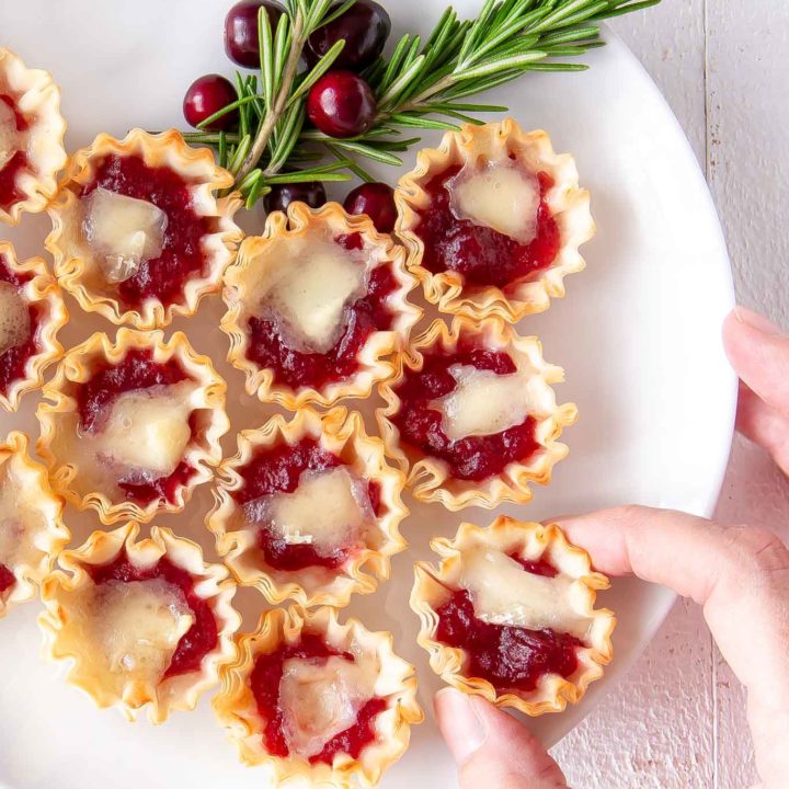 cranberry orange brie tarts on a plate with a hand taking one off