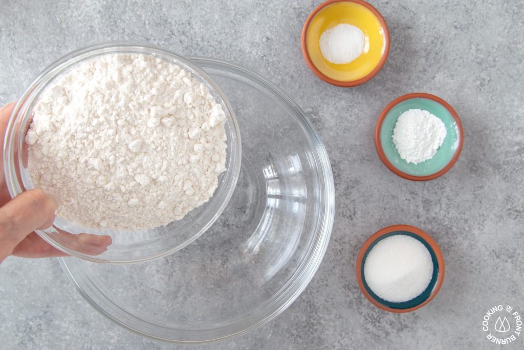 pouring flour in a glass bowl to make mini pancakes