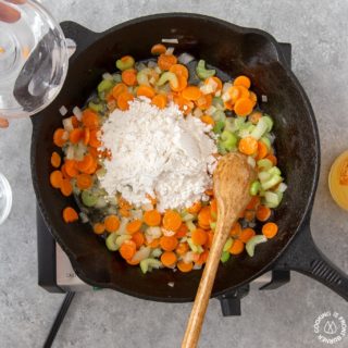 adding flour to a skillet over sauteed veggies for chicken pot pie