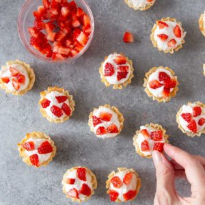 a hand placing strawberries on cheesecake tarts