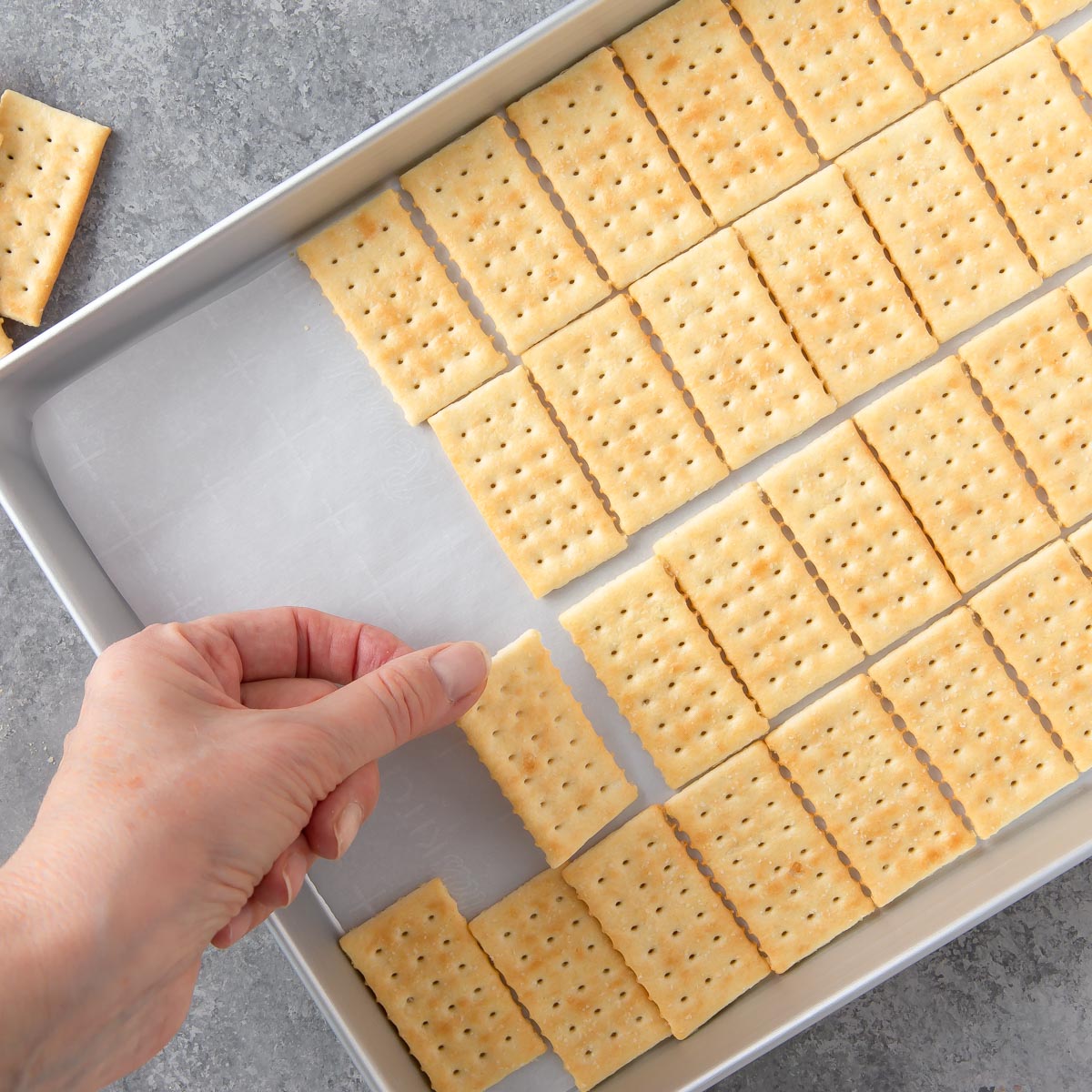 jelly roll pan with a hand placing crackers on it