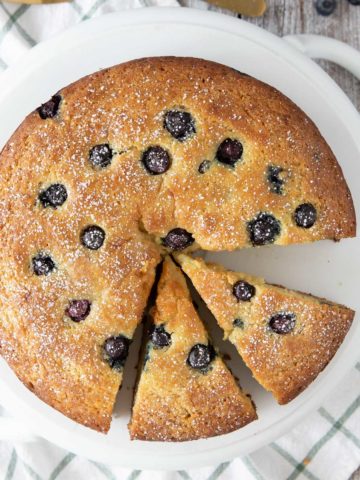 lemon blueberry ricotta cake with 2 slices cut out on a cake plate