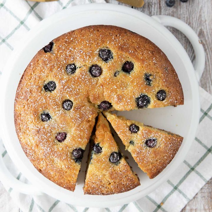 lemon blueberry ricotta cake with 2 slices cut out on a cake plate