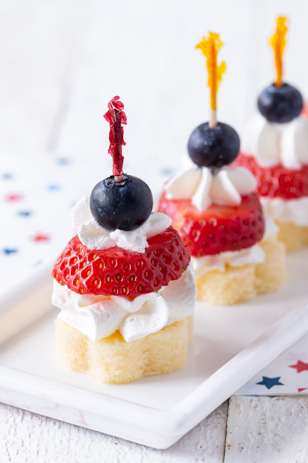 two pound cake stackers with strawberries, cool whip and a blueberry on a plate