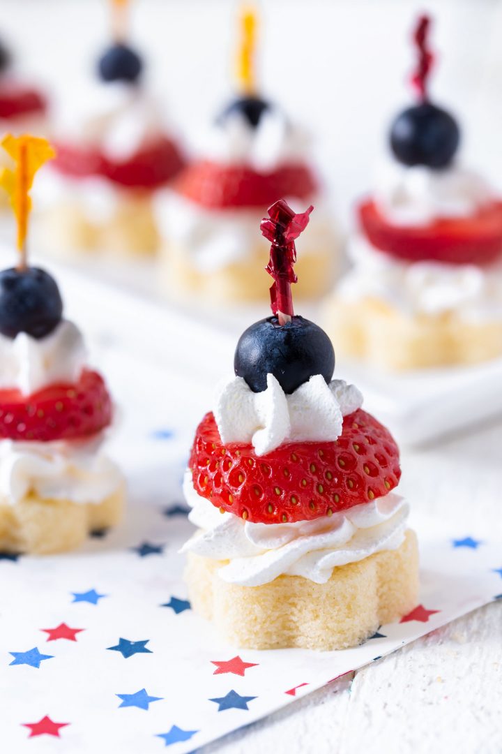 small pound cake pieces topped with cool whip, a slice of strawberry and a blueberry held together by a toothpick