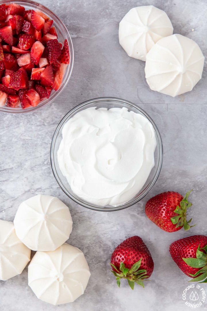 ingredients needed to make strawberry shoothers - fresh strawberries, mernigue cookies and cool whip in bowl on a board
