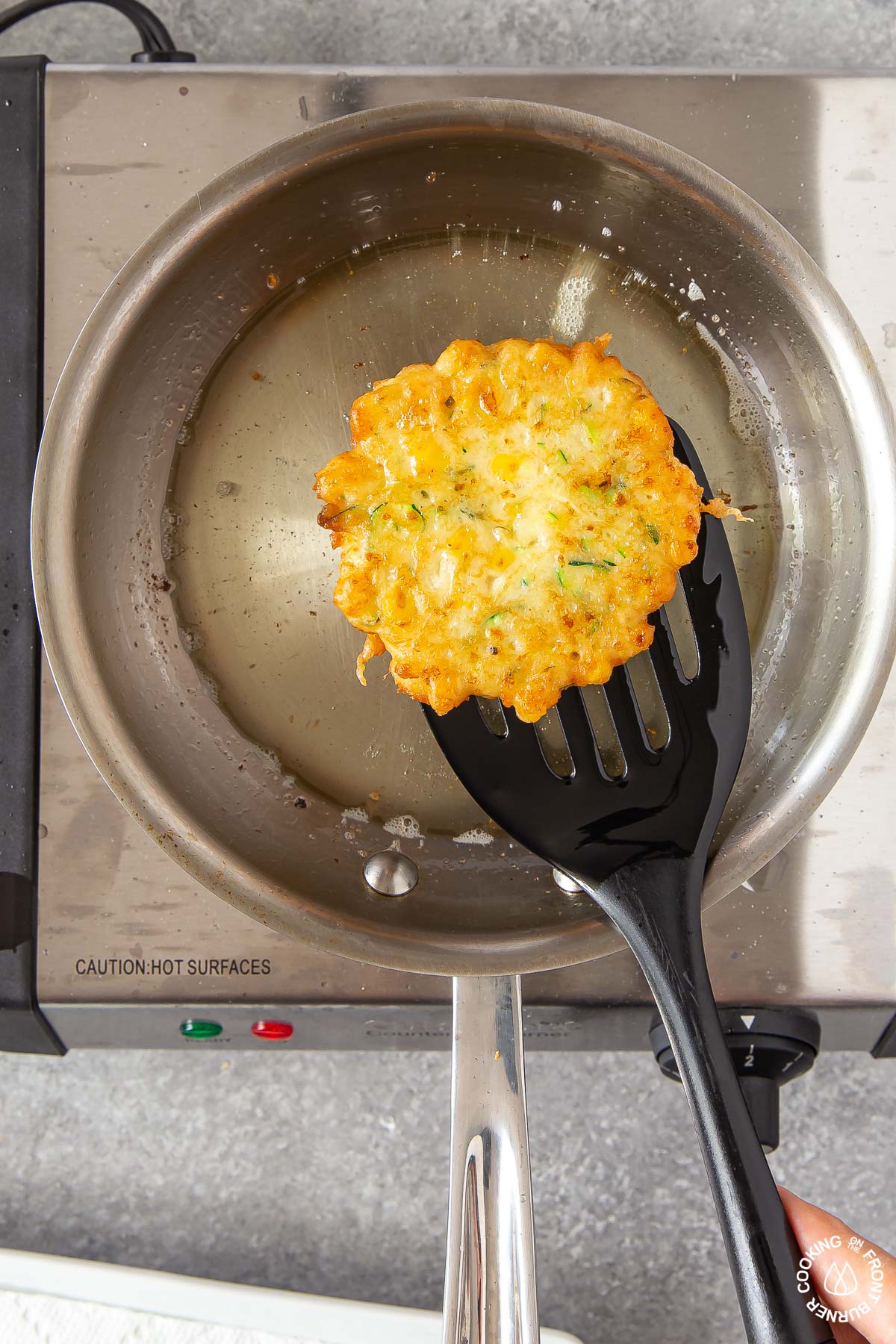 removing a fried zucchini corn fritter from skillet with a spatula