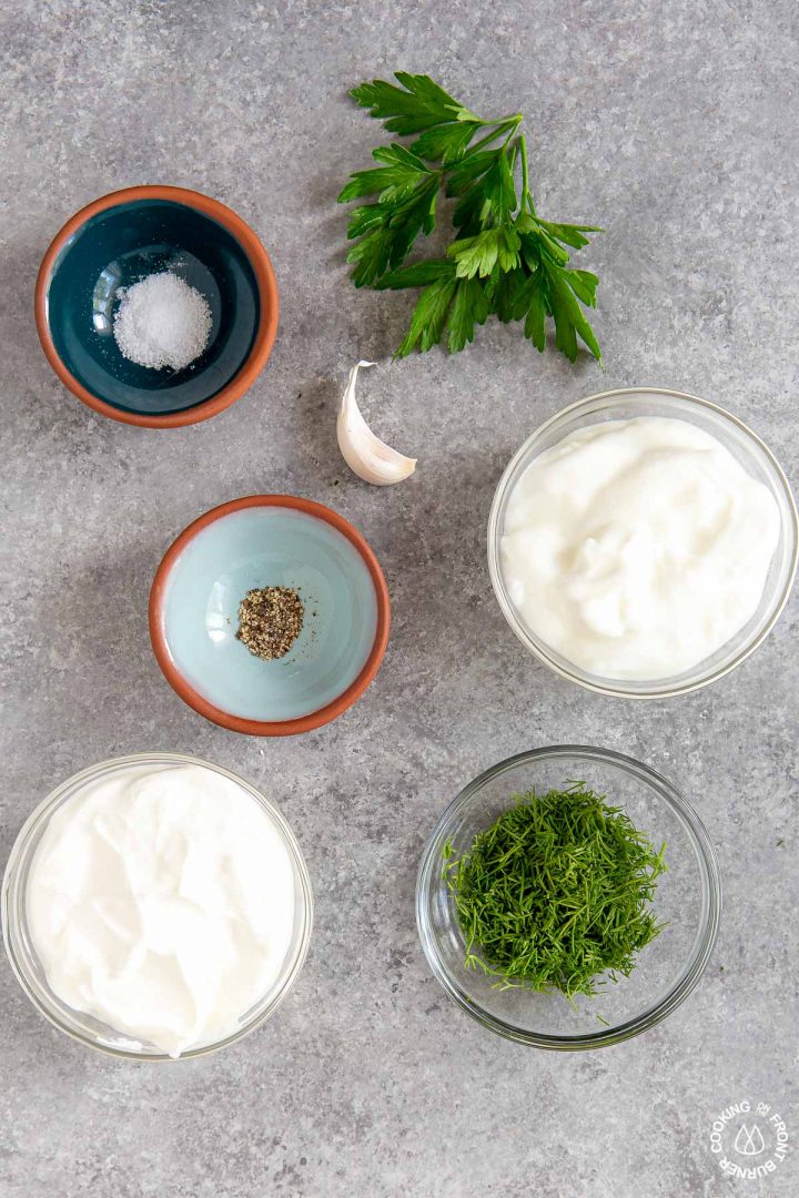 bowls of sour cream, plain yogurt, salt, pepper, dill, parsley garlic clove