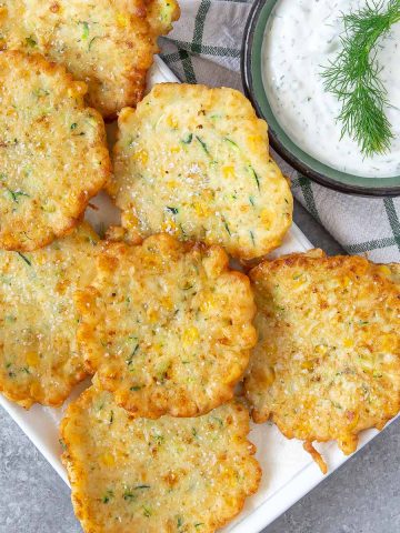 a plate with friend corn zucchini fritters and a side of dill dip