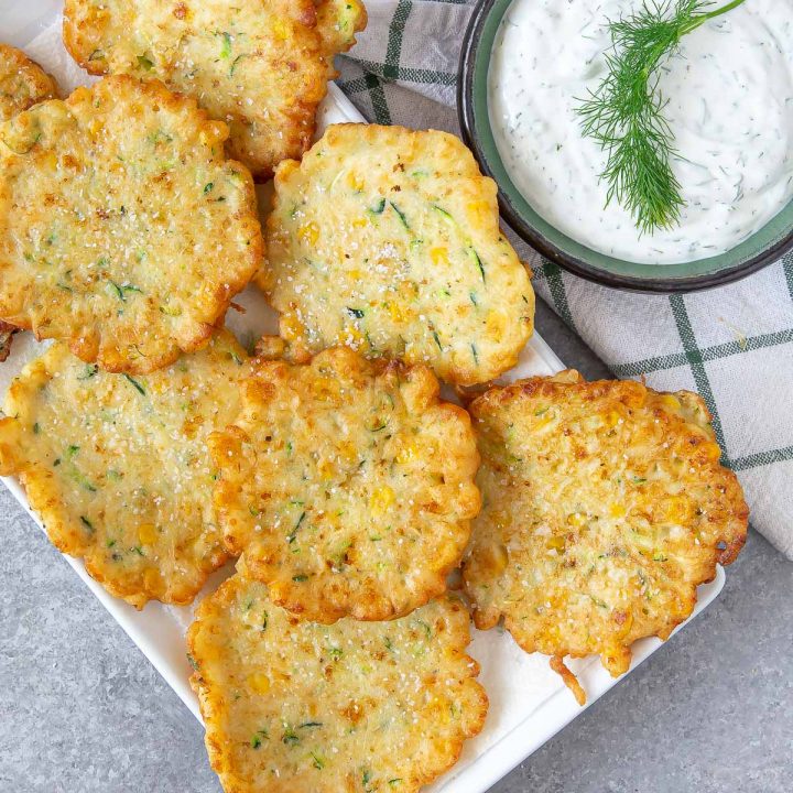 a plate with friend corn zucchini fritters and a side of dill dip