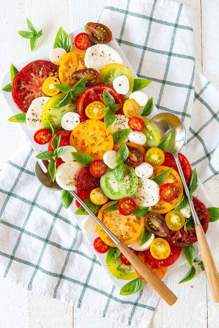 caprese salad on a white platter with a big fork and spoon