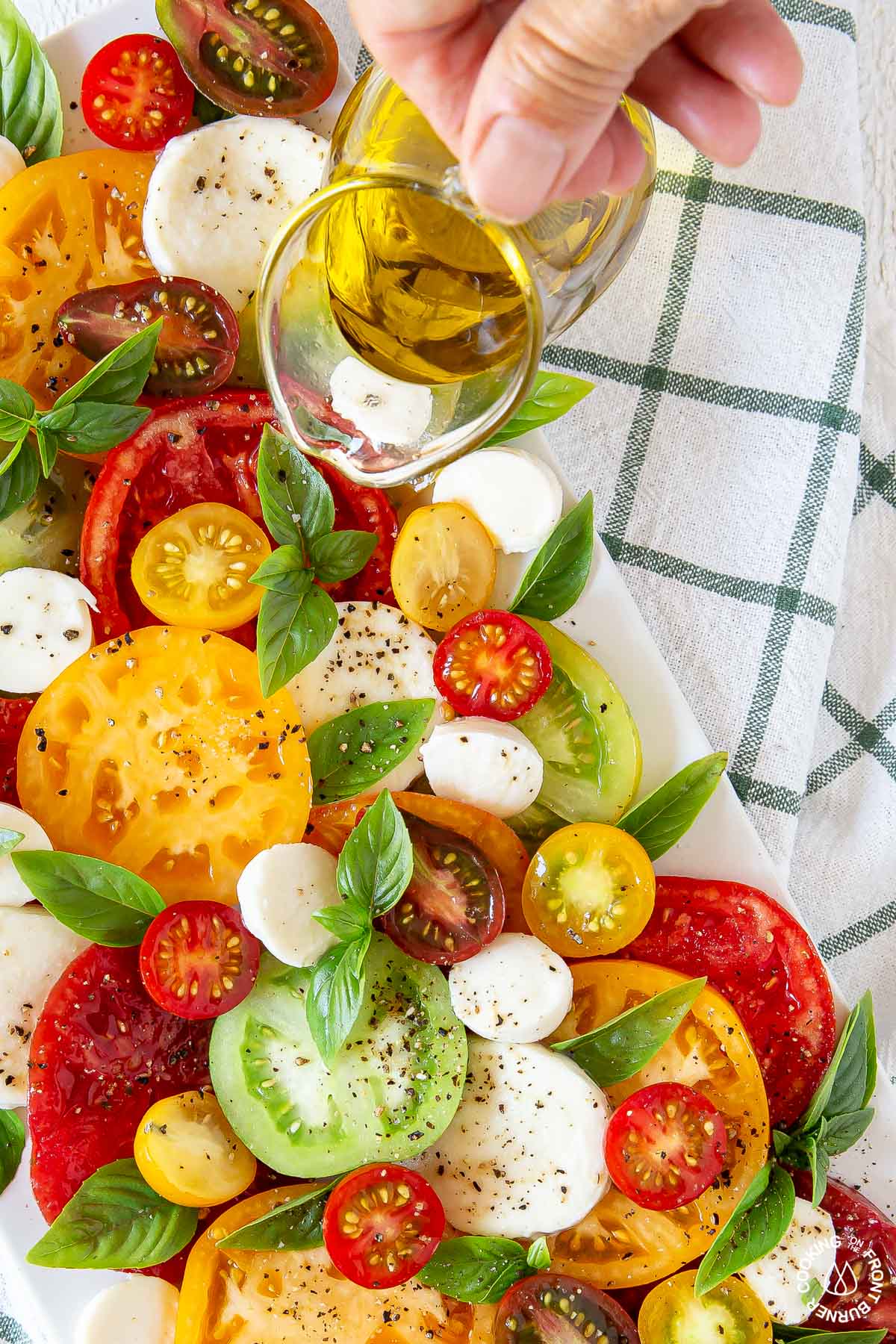 drizzling olive oil over a caprese salad on a white platter