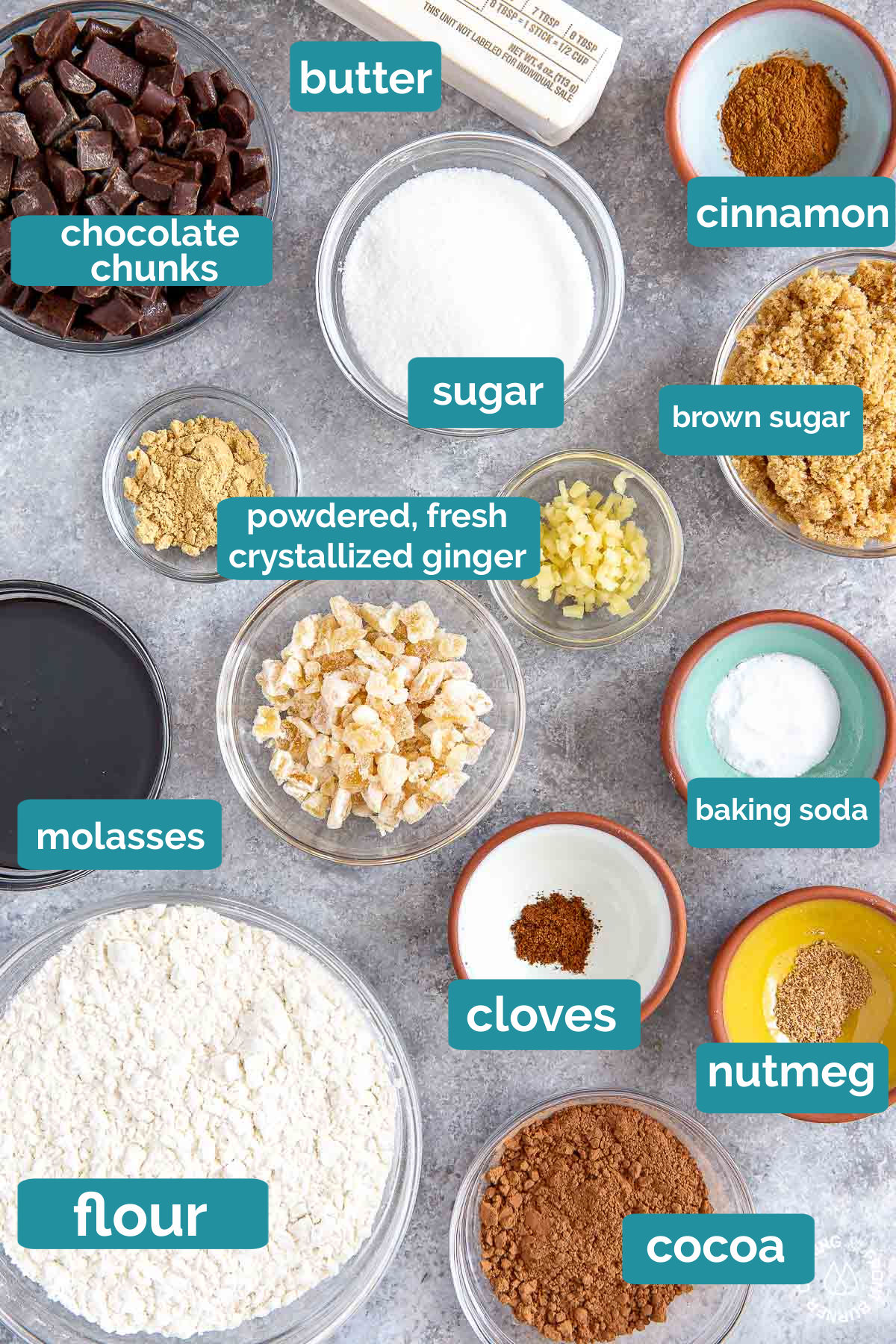 a board with flour, chocolate chunks, molasses, ginger, cinnamon, brown sugar, cloves and nutmeg in bowls