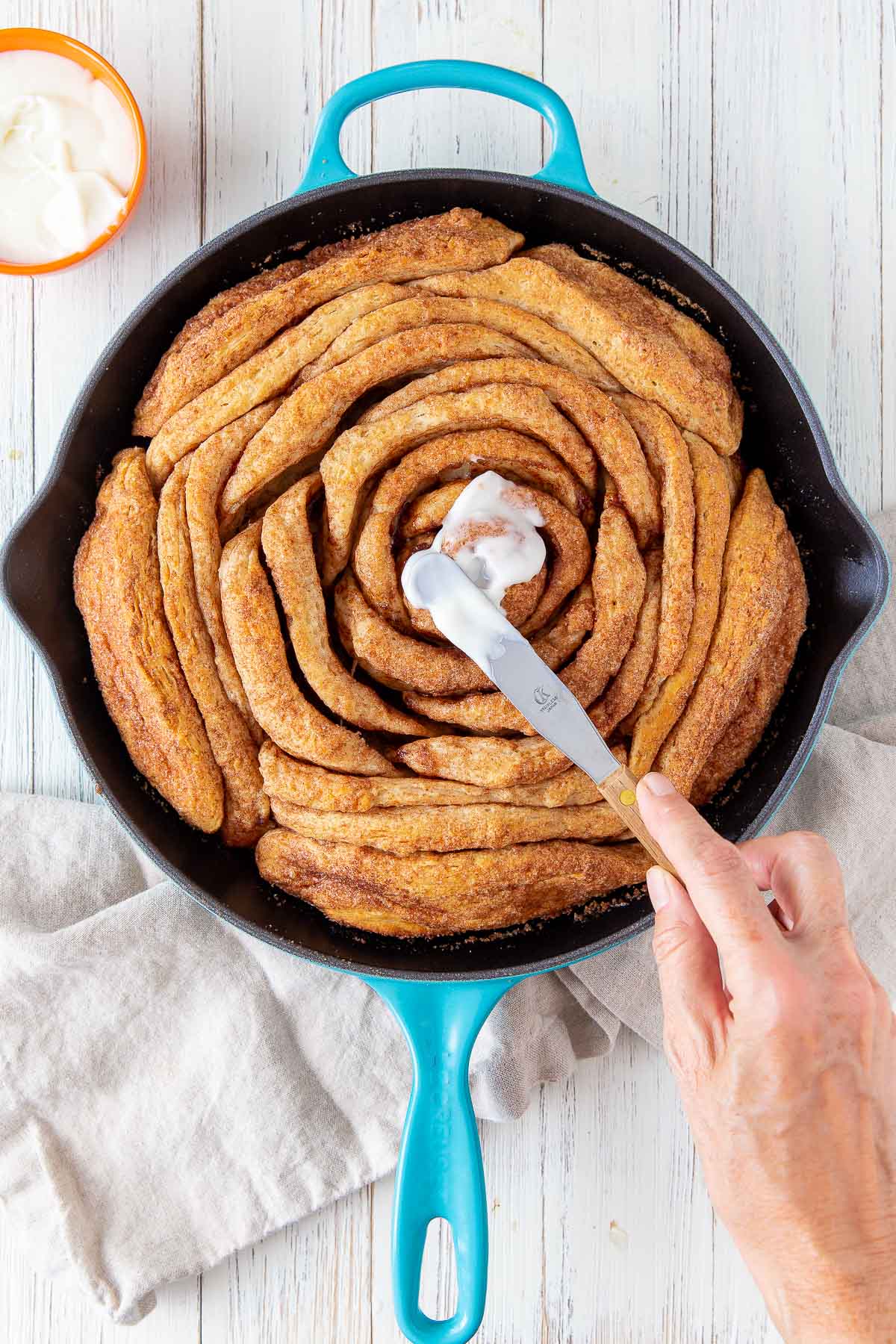 spreading cream cheese frosting on a baked skillet cinnamon roll