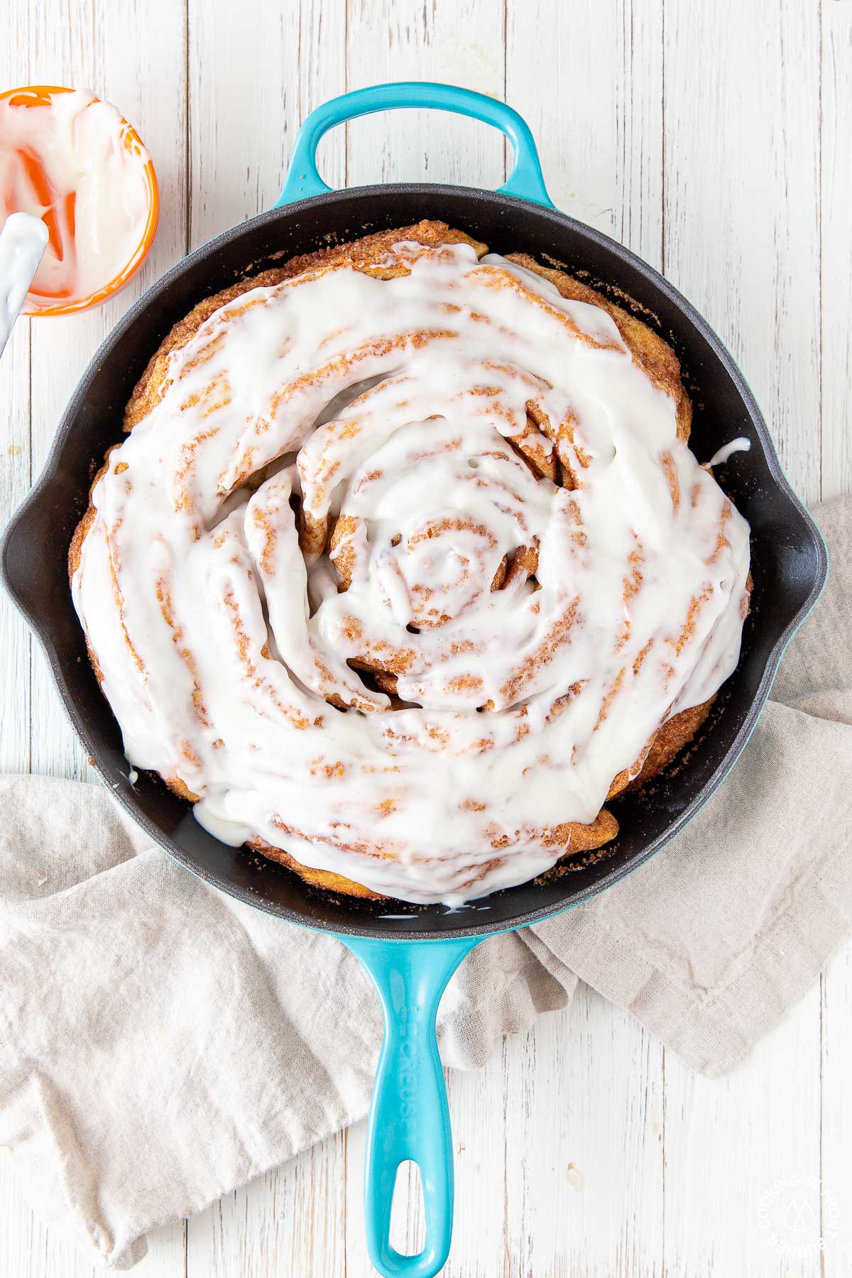 a skillet with cinnamon rolls topped with cream cheese frosting