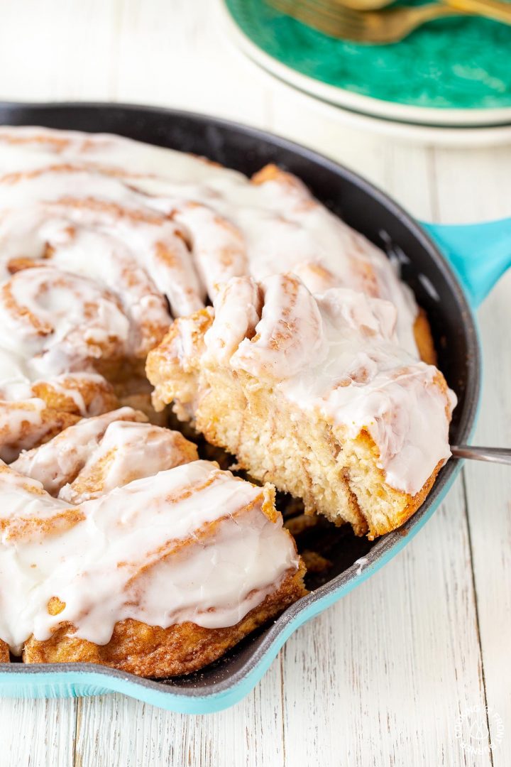 a slice of a skillet cinnamon roll on a spatula coming out of a skillet